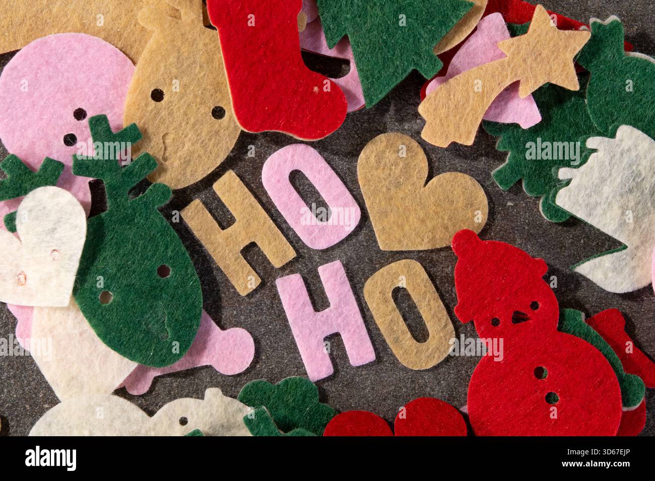 Bunte Filzausschnitte auf dunkler Oberfläche zeigen Weihnachtsmotive wie Rentiere, Strümpfe und Schneemänner. Diese Szene ist perfekt für einen Urlaub Stockfoto