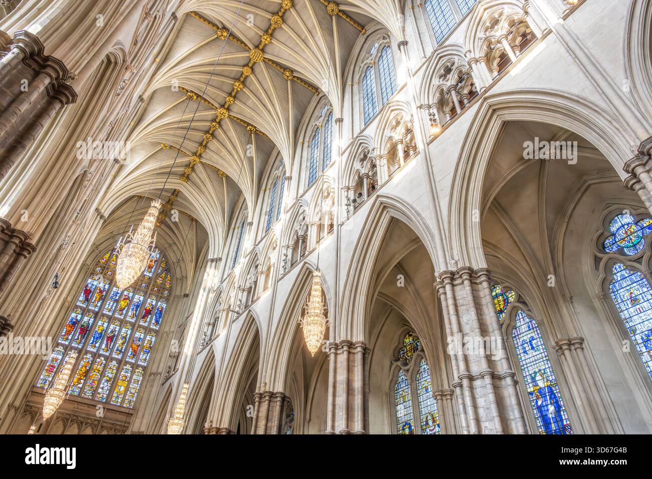 Entdecken Sie die komplizierte gotische Architektur der Westminster Abbey mit atemberaubenden Bögen, detaillierten Buntglasfenstern und herrlichen Kronleuchtern, die das historische Innere beleuchten. Stockfoto