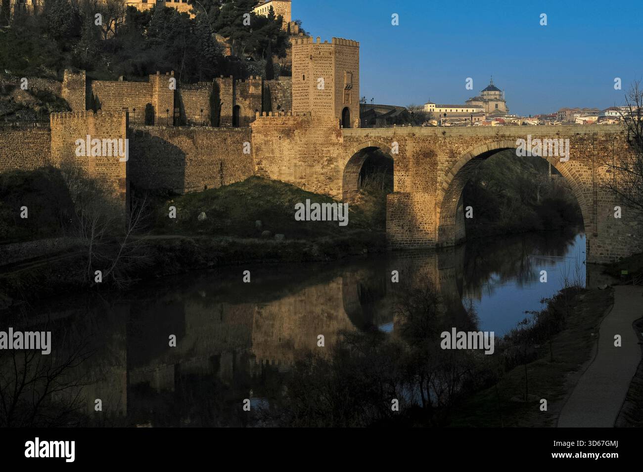 Römische und mittelalterliche Puente de Alcántara oder Alcántara-Brücke, die sich im ruhigen Fluss Tejo unter der UNESCO-Weltkulturerbestätte Toledo, Kastilien-La Mancha, Zentralspanien, spiegelt. Erbaut für das römische Municipium von Toletum, von den Westgoten genutzt und von den Mauren wiederaufgebaut, mit dem Westtor-Turm mit königlichen Wappen der spanischen katholischen Monarchen aus dem 15. Jahrhundert, Ferdinand und Isabella. Stockfoto