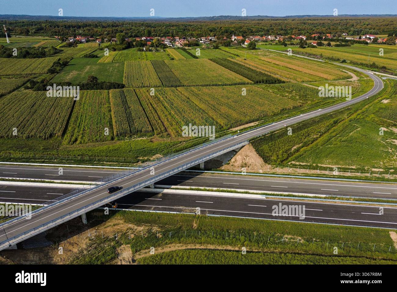 Aus der Vogelperspektive einer Betonbrücke, die einen langen Schatten über eine mehrspurige Autobahn wirft, umgeben von lebhaften grünen Feldern und üppigen Wäldern, Zagreb, Kroatien. Stockfoto
