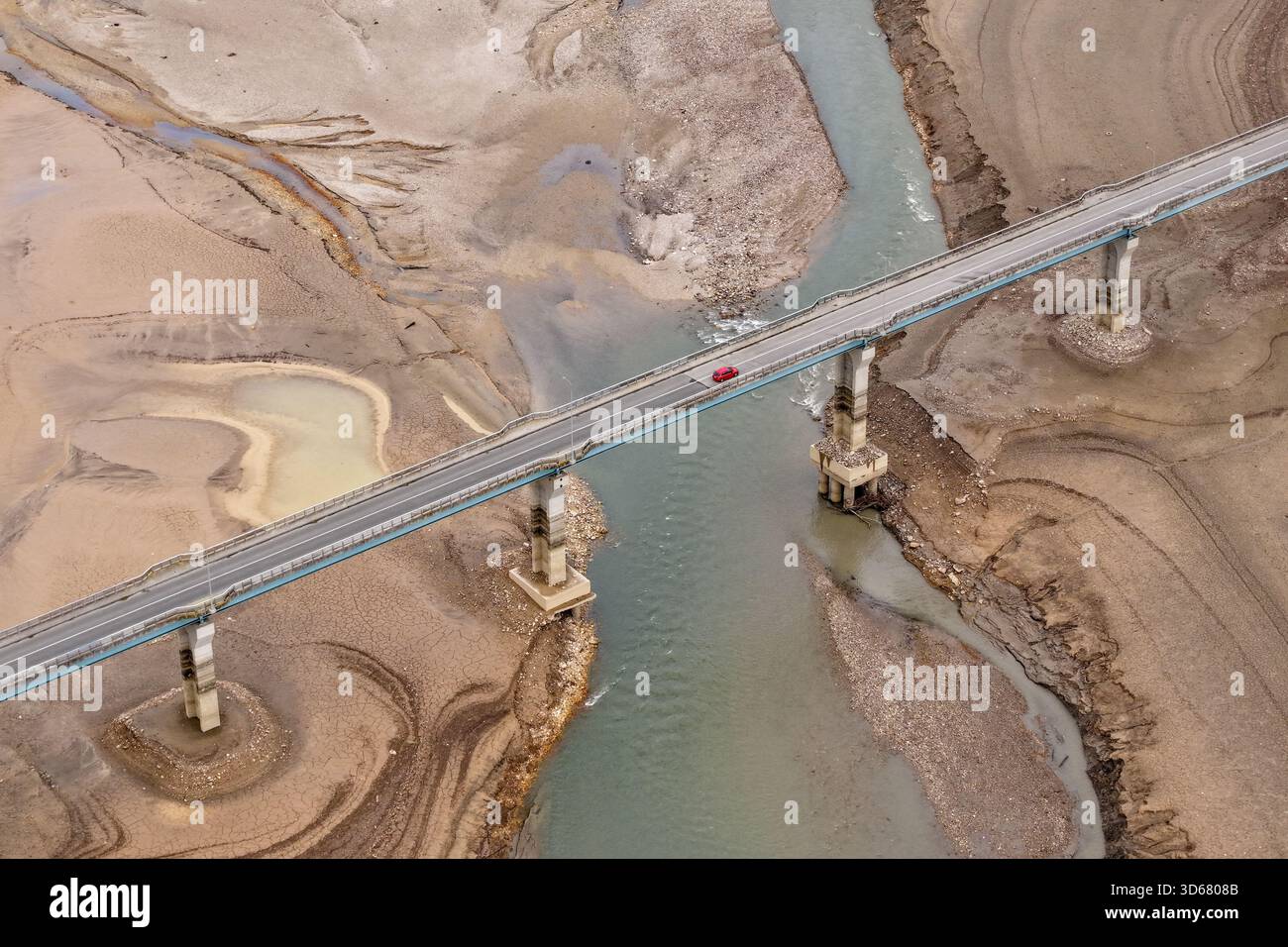 Aus der Vogelperspektive überquert ein einsames rotes Auto die Brücke über ein trockenes Flussbett und steht in starkem Kontrast zur verdorbenen Landschaft, Lisičići, Föderation von Bosn Stockfoto