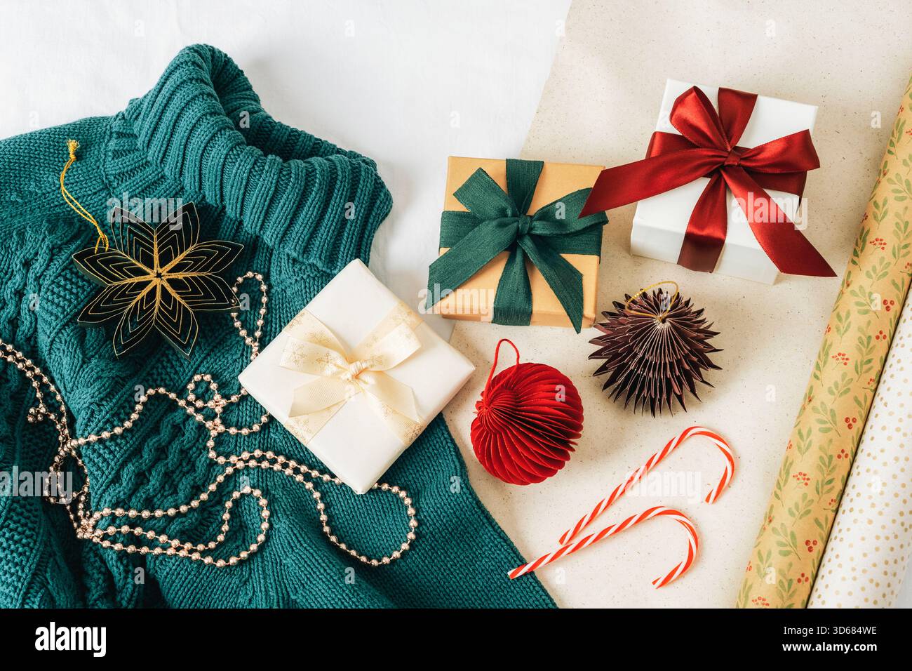Ansicht von oben auf Weihnachtsgeschenken auf blauem Strickpullover mit Ornamenten und Geschenkpapier auf weißem Hintergrund. Neujahr- oder Weihnachtsferien-Konzept, fla Stockfoto