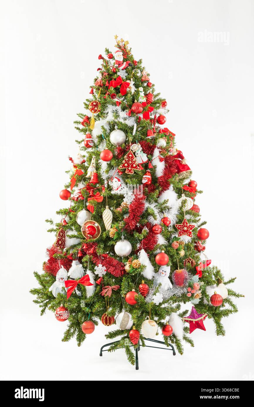 Festlicher, künstlicher grüner Weihnachtsbaum mit Rot- und Weißmotiv und einer Auswahl an Dekorationen über weiß zur Feier der Weihnachtszeit Stockfoto