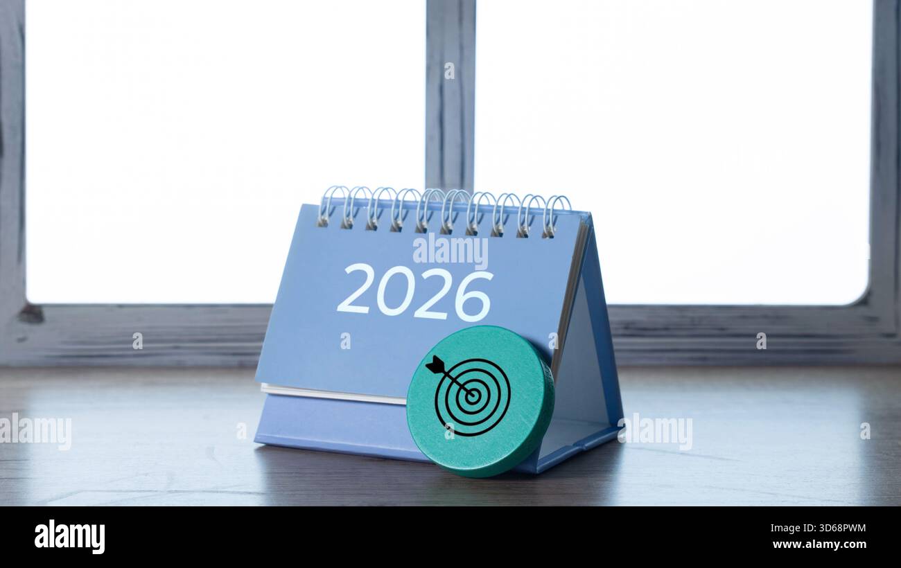 Tischkalender mit dem Jahr 2026 und einem grünen Zielsymbol, das Ziele und Planung auf einem Holztisch symbolisiert. Stockfoto