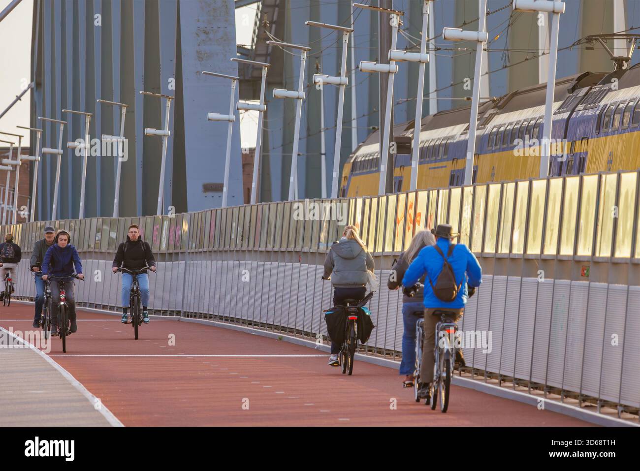 Nijmegen, Niederlande - 12. November 2025: Menschen radeln neben einem vorbeifahrenden Personenzug auf einer Brücke in Nijmegen, Niederlande Stockfoto