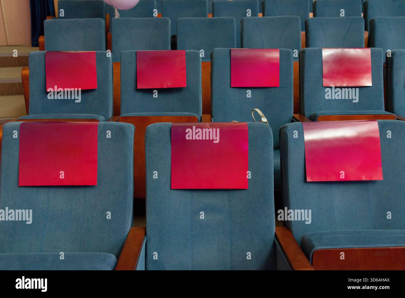 Eine Anordnung leerer blauer Theatersitze, die jeweils mit einer auffälligen roten Tafel verziert sind. Dieser Bildkontrast und die Symmetrie in einem modernen Auditorium Stockfoto