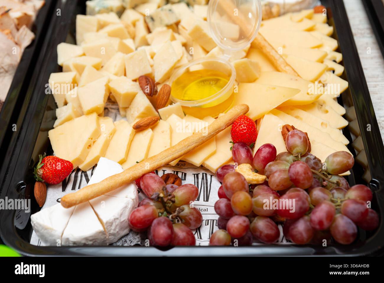 Eine appetitliche Gourmet-Käseplatte mit verschiedenen Käsesorten, frischen Trauben, Mandeln und Erdbeeren. Perfekt für Versammlungen oder besondere Gelegenheiten Stockfoto