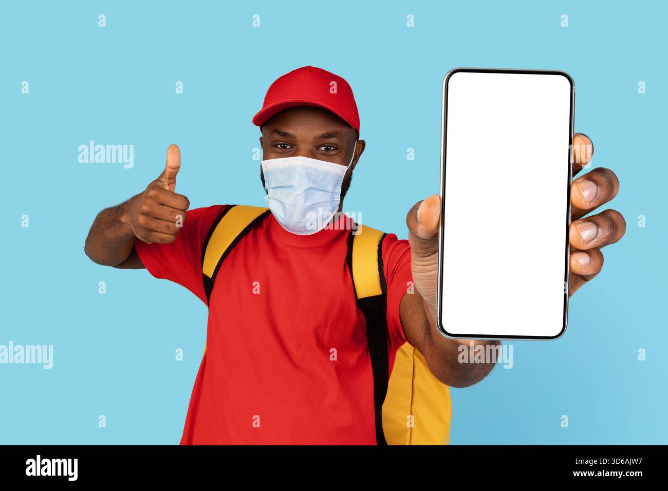 Sichere Lebensmittelzustellung. Schwarzer Kurier Mann Trägt Medizinische Maske Zeigt Blank Smartphone Stockfoto