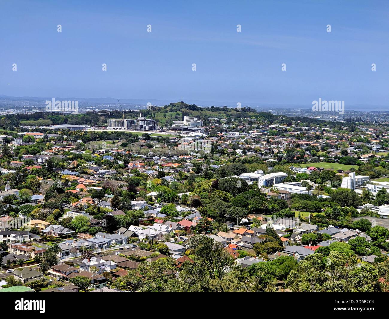 Breiter erhöhter Blick auf die Vororte von Auckland mit Wohnhäusern, Grünflächen und fernen Hügeln unter einem hellblauen Himmel. Stockfoto