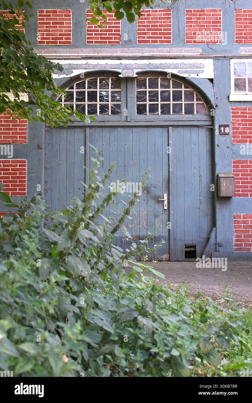 Detailansicht einer historischen Fachwerkfassade mit einer weißen Doppeltür, gemauerten Einfüllpaneelen und einer ornamentalen Inschrift. Stockfoto