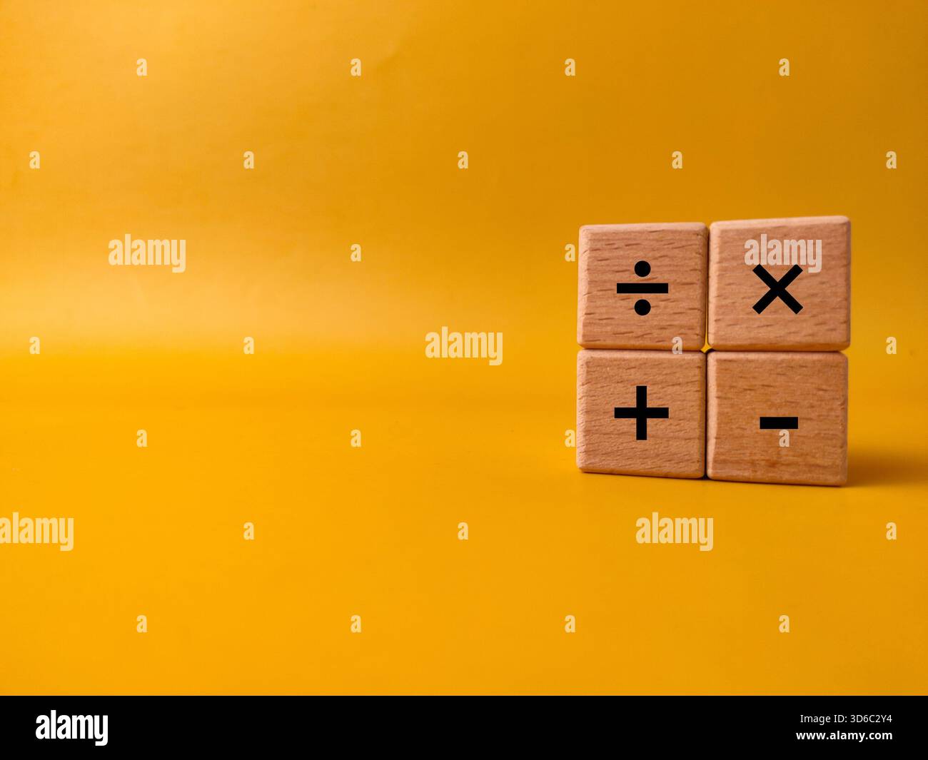 Das Bild zeigt vier Holzblöcke mit grundlegenden mathematischen Betriebssymbolen auf gelbem Hintergrund. Stockfoto