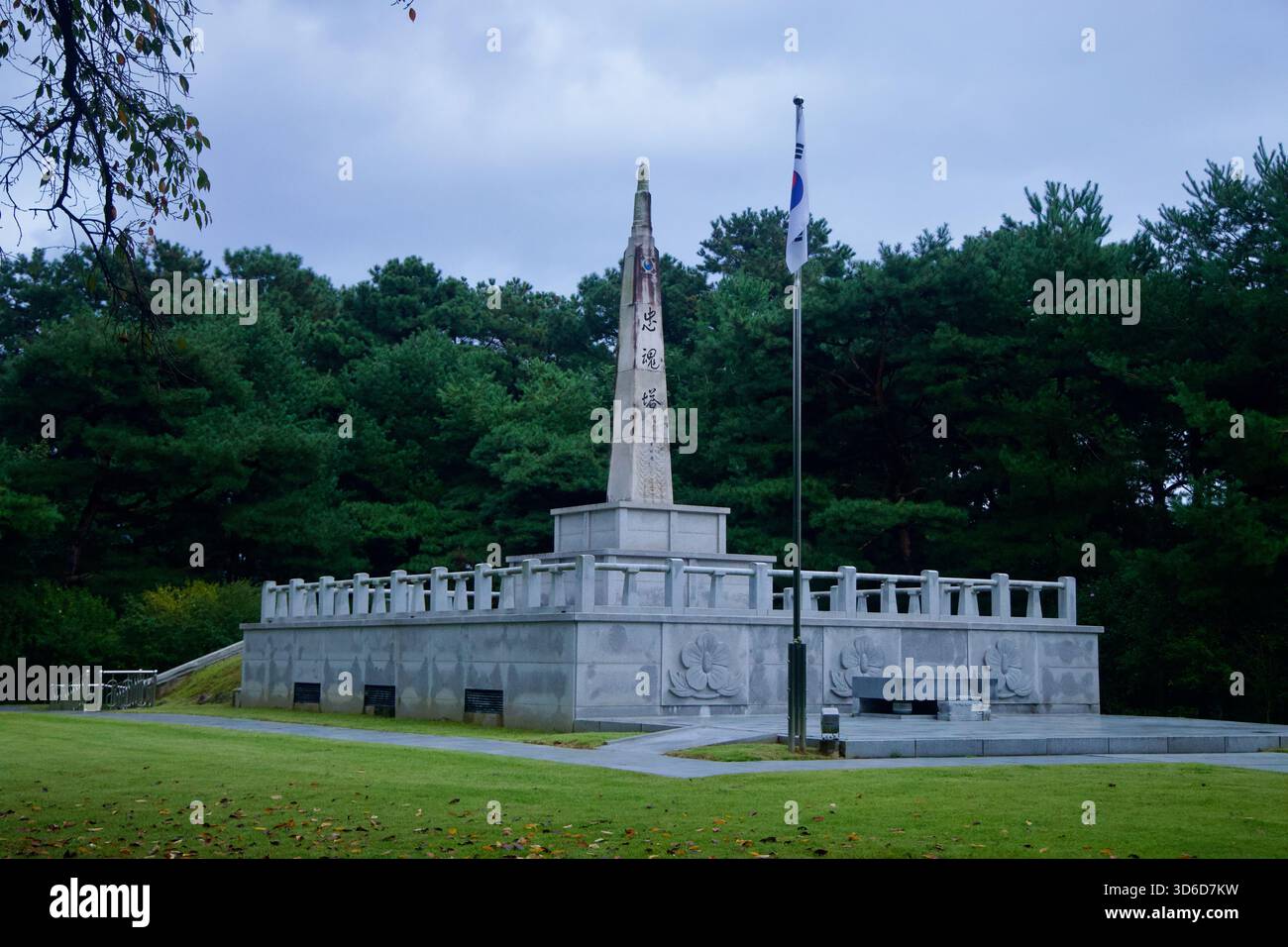 Ein Granit-Gedenkturm mit koreanischer Inschrift erhebt sich neben einem Fahnenmast im Tangeumdae Park. General Sin Rip Monuments, auf einer erhöhten Plattform. Stockfoto