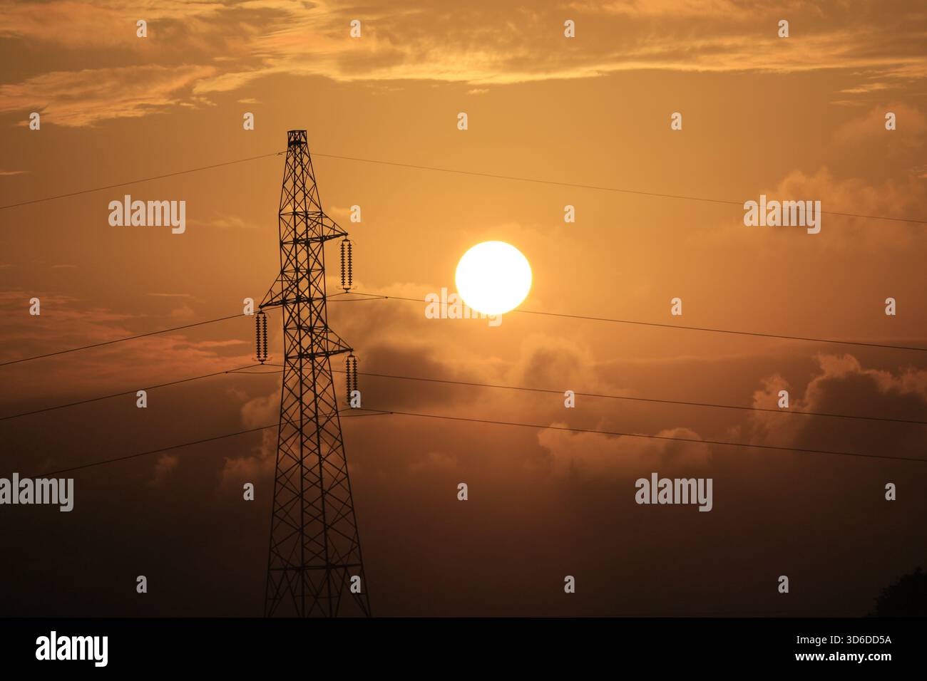 Die Silhouette der Stromlinie vor einem feurigen Sonnenuntergang, der den Tag mit warmem Sonnenlicht der goldenen Stunde umschmeichelt Stockfoto