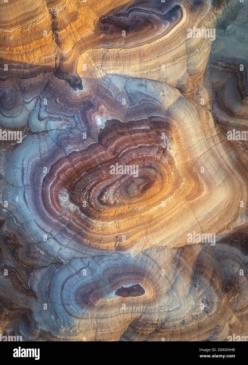Aus der Vogelperspektive auf die abstrakte Leinwand der Natur, wo sich wirbelnde Bänder aus Ocker, Sienna und Lavendel in faszinierenden Mustern zusammenfügen, Hanksville, Utah, Unite Stockfoto