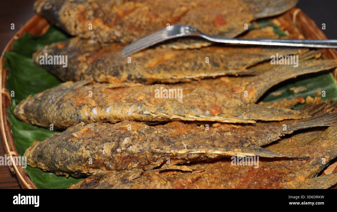 Knuspriger gebratener Fisch auf Bananenblättern in einem Bambusteller serviert. Traditionelle asiatische Meeresfrüchte-Küche mit goldener Textur, knuspriger Haut und authentischem Homema Stockfoto
