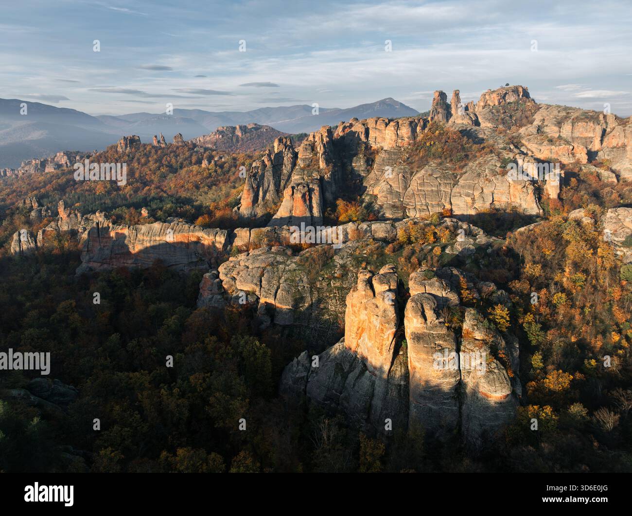 Aus der Vogelperspektive der zerklüfteten Belogradchik Rocks, deren orangene Farbtöne lange Schatten über den herbstlich gefärbten Wäldern darunter werfen, Belogradchik, Vidin, Bulgar Stockfoto