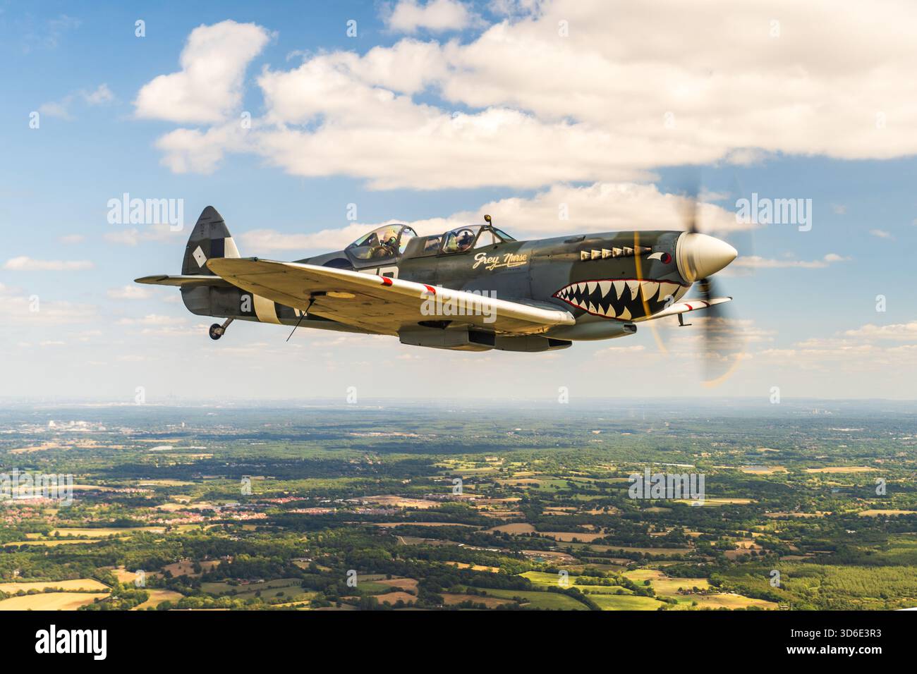 Hampshire, England - 09. August 2025: Aus der Vogelperspektive eines alten Kampfflugzeugs, das über den üppigen, grünen Flickenteppichfeldern und der fernen Stadtlandschaft unter einem br Stockfoto