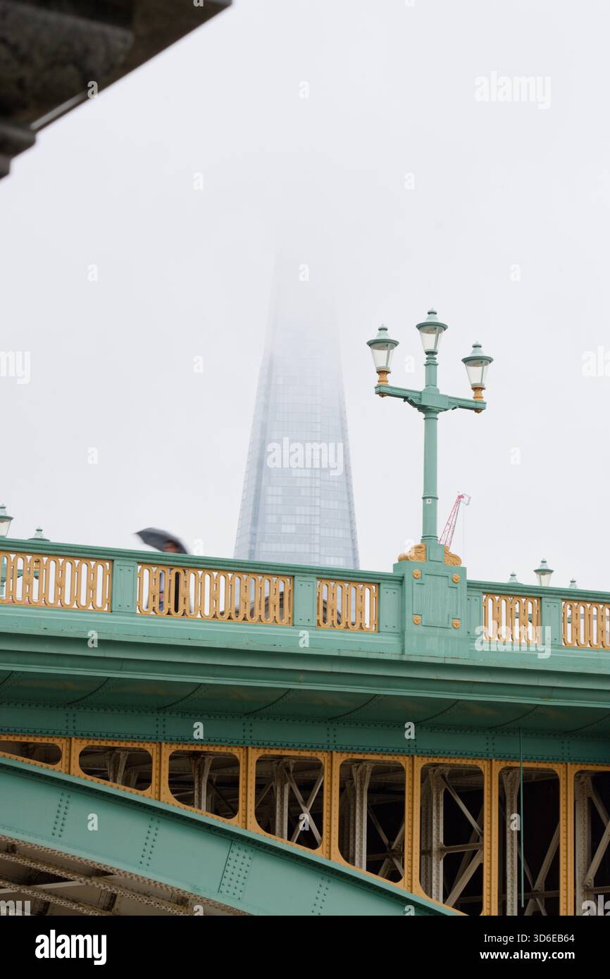 Eine regnerische Hauptstadt von London an einem nassen Tag. Neblig und regnerisch! Eine Person unter einem Bach, der die Southwark Bridge überquert. Das Scherbengebäude in Nebel. Stockfoto