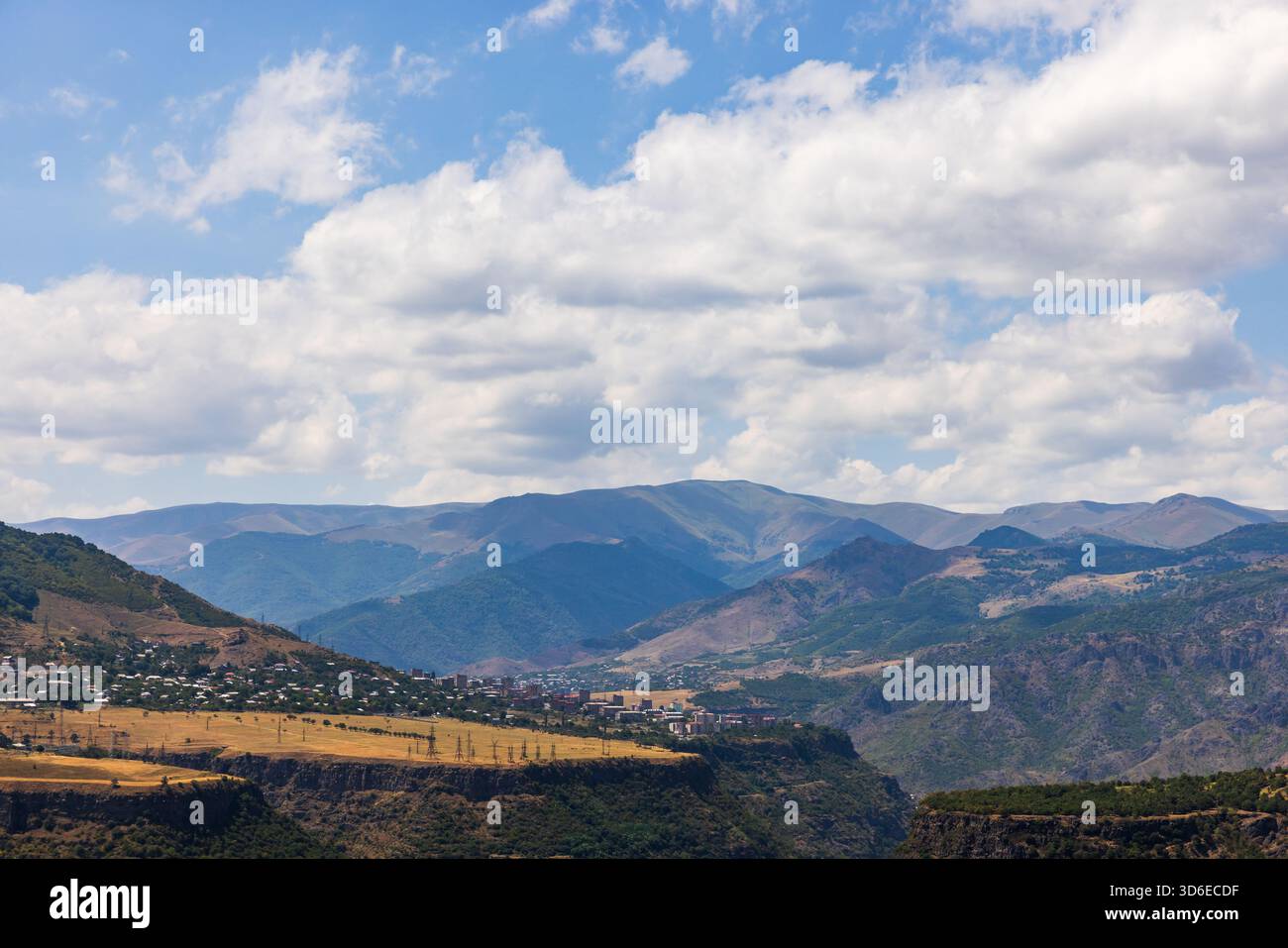Weitläufige Landschaft mit einem Dorf im Tal entlang zerklüfteter Berge, einem hellblauen Himmel mit weißen Wolken und mehrschichtigen Hügeln. Alaverdi, Provinz Lori Stockfoto