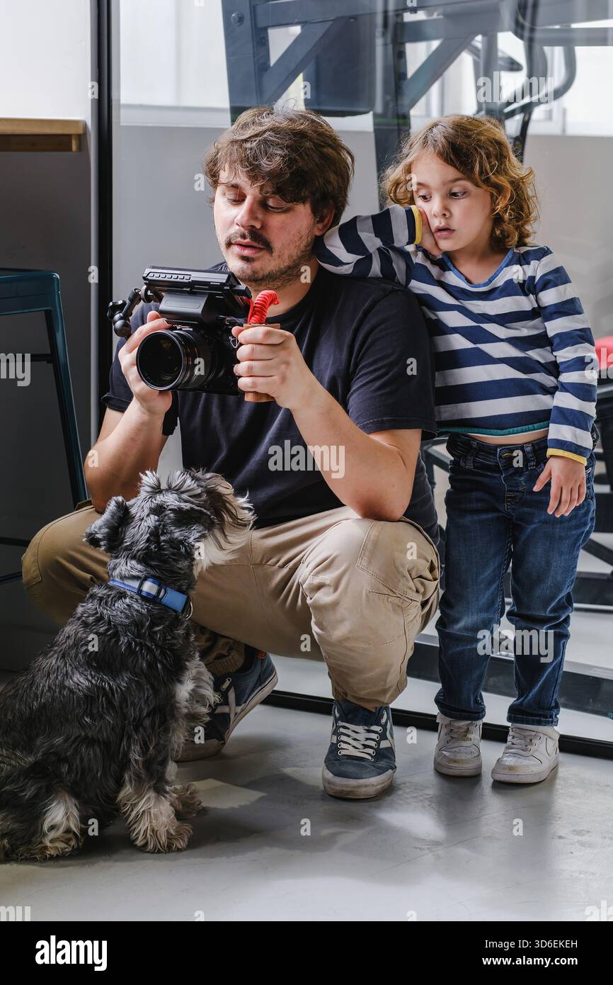Vater und Kind werden von ihrem Hund begleitet, um Aufnahmen auf einer professionellen Videokamera in einem Innenbereich zu lesen Stockfoto