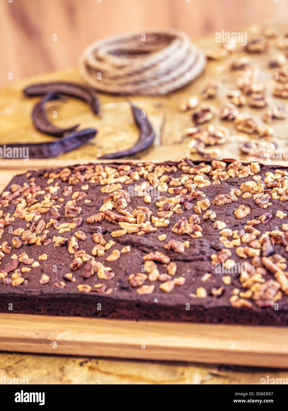Reichhaltiger Schokoladenkuchen, der großzügig mit knusprigen Walnüssen belegt ist, auf einem rustikalen Holzschneidebrett ausgestellt, mit Hufeisen und Seilen im Stockfoto