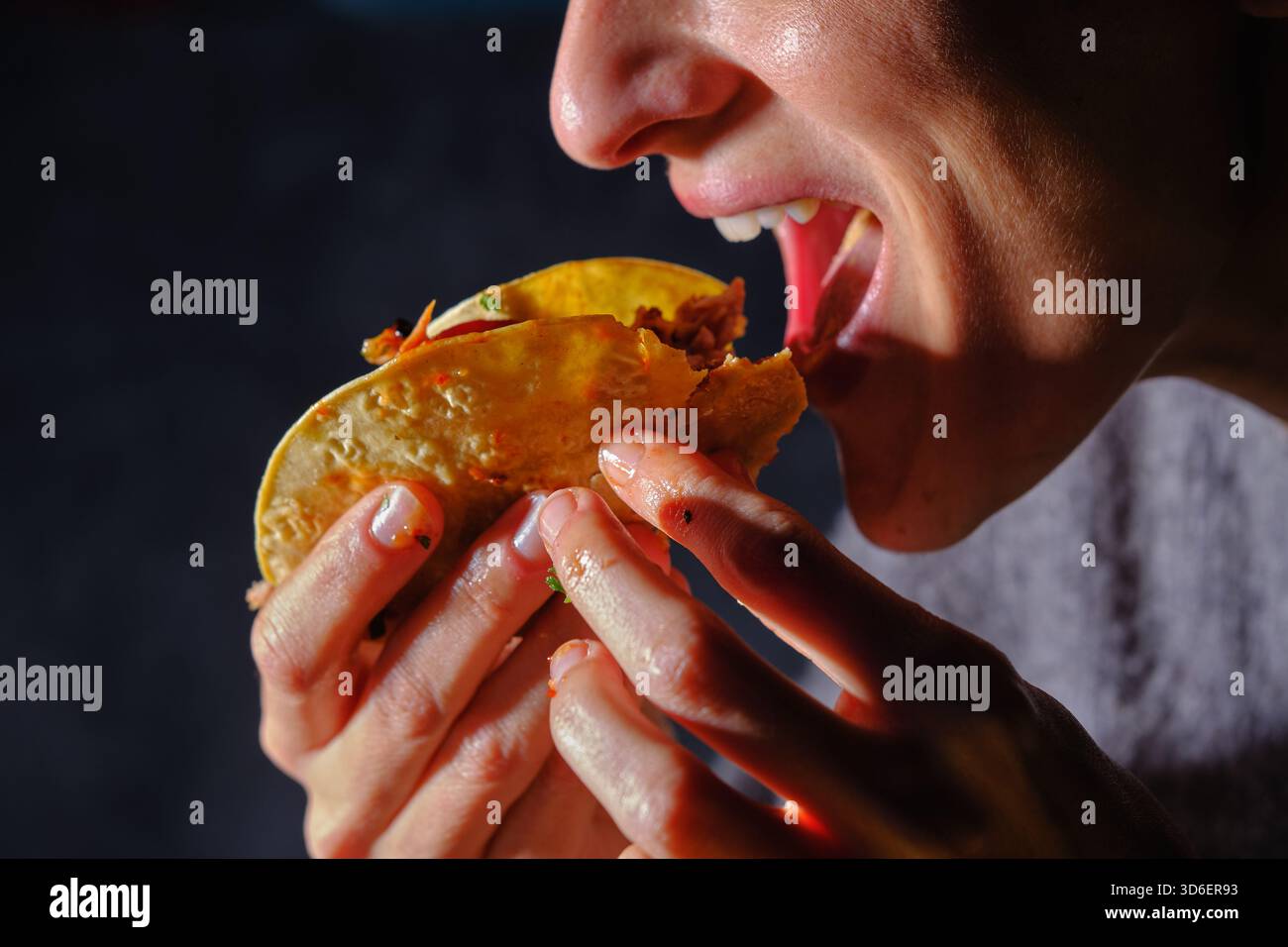 Ein zugeschnittenes, nicht erkennbares Nahaufnahme-Bild, das eine Frau einfängt, während sie in einen geschmackvollen Ripptako beißt. Ihre Finger greifen den Taco fest und heben den hervor Stockfoto