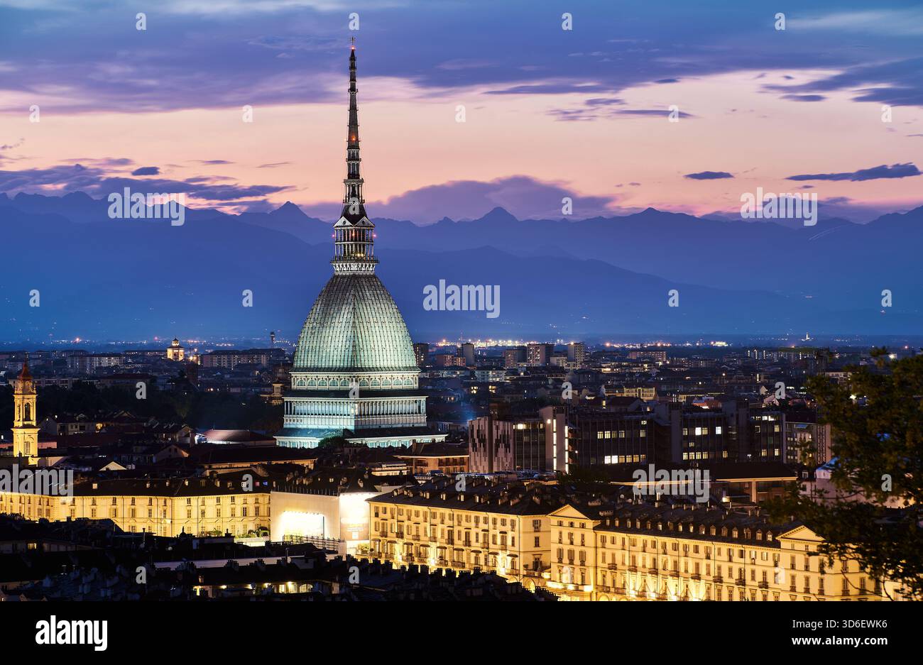 Die Skyline von Turin leuchtet in der Abenddämmerung, dominiert von der berühmten Mole Antonelliana, mit eleganten historischen Gebäuden darunter und der Silhouette der Alpen Stockfoto