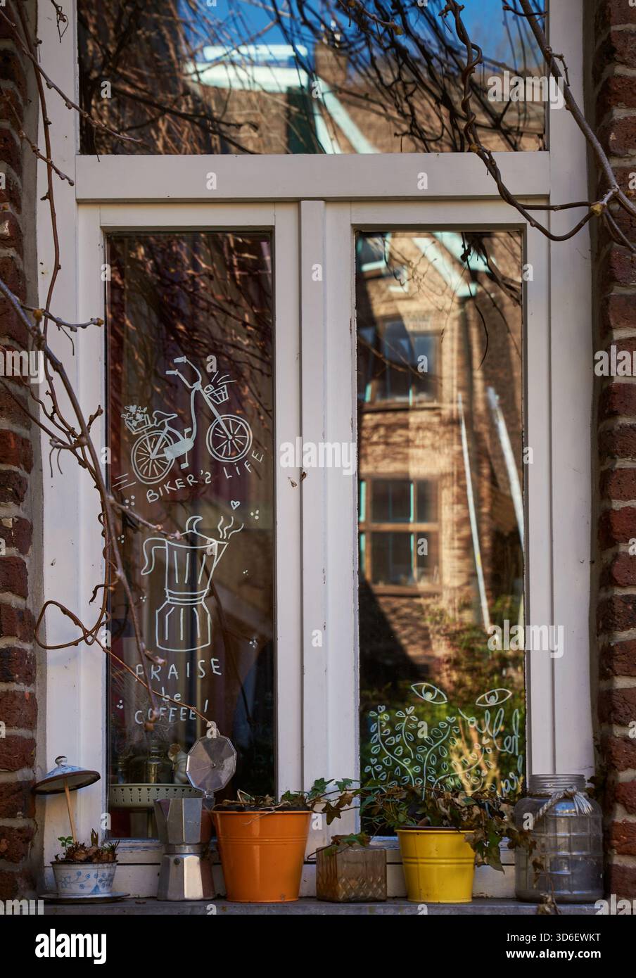 Malerisches Fenster mit gezeichneter Kunst eines Fahrrads und Kaffees, Vintage Töpfen, Efeu und warme Reflexe, die heimeligen Komfort, Kreativität und einen Hauch von Natur verbinden Stockfoto