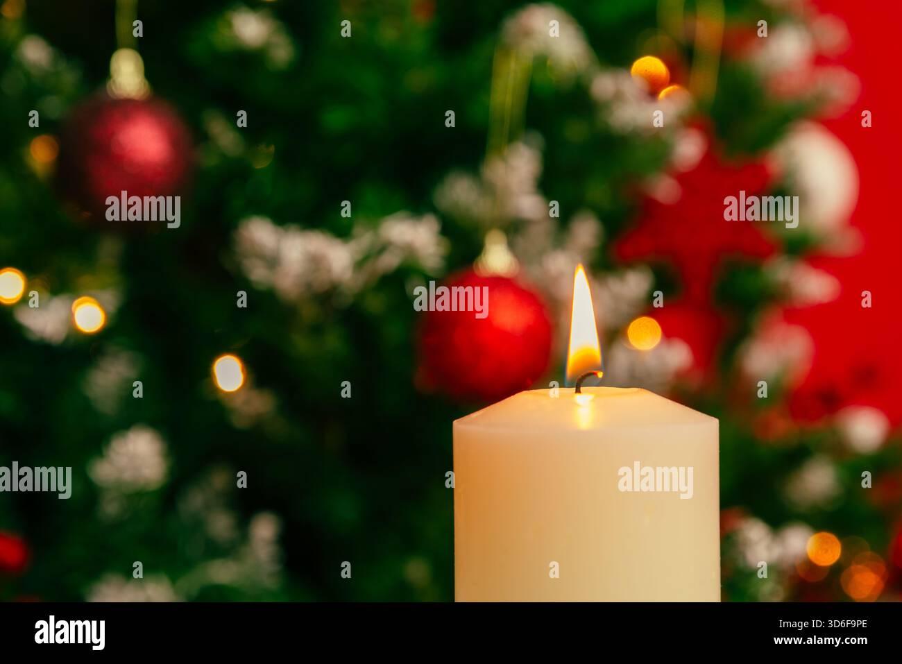 Weihnachtliche Kerzenflamme in Nahaufnahme mit hellen Weihnachtsleuchtern und Dekorationen, die dahinter sanft verschwimmen, sorgen für warme saisonale Themen Stockfoto