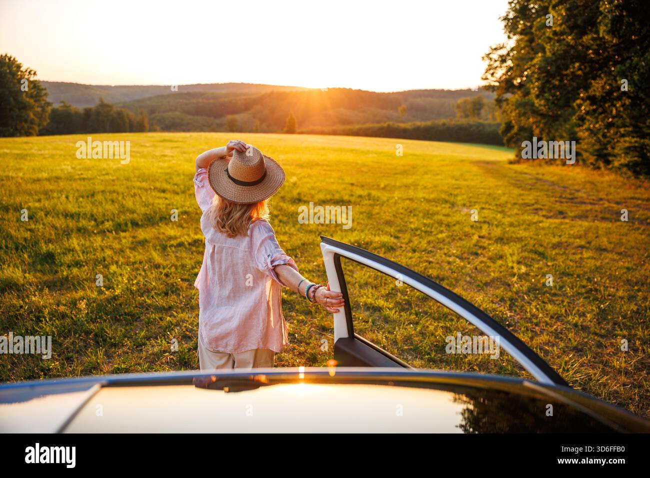 Reisen Sie im Sommerurlaub mit dem Auto. Sorglose Frau, die den Sonnenuntergang während eines Roadtrips in idyllischer Landschaft genießt. Freude am Freiheitsreisen Stockfoto