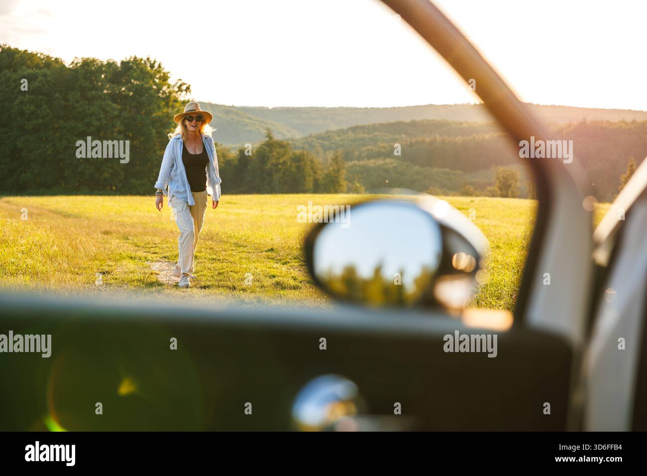 Glückliche lächelnde Frau, die den Sonnenuntergang während des Roadtrip-Stopps genießt. Blick durch das Autofenster. Reisen Sie im Sommerurlaub Stockfoto