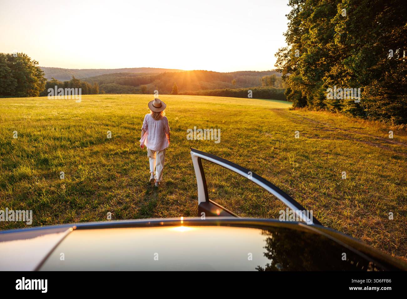 Frau, die vom Auto weg in das Sommersonnenfeld geht. Konzept von Freiheit, Eskapismus und Reisefreude Stockfoto