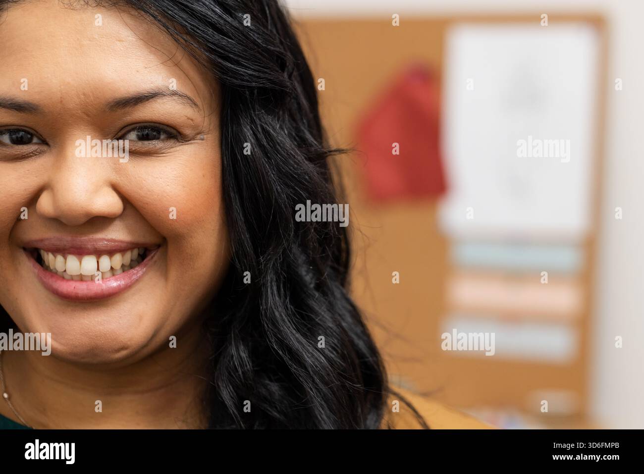 Asiatische Frau mit Senfpullover lächelt im Büro mit Korkbrett und Haftnotizen, Kopierraum Stockfoto