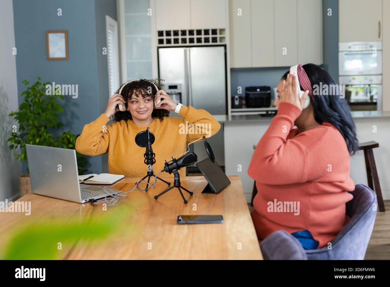 Afroamerikanische Freundinnen passen Kopfhörer an und testen Mikrofone am Küchentisch Stockfoto