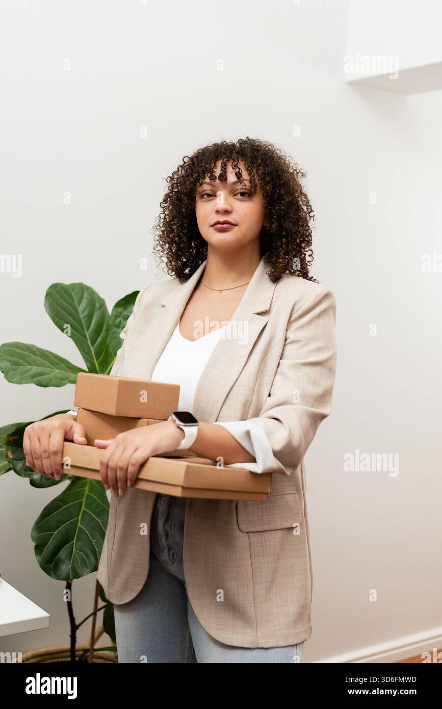 Afroamerikanerin mit Blazer und Smartwatch, die Versandkartons im Büro bei Feigenwerk hält Stockfoto