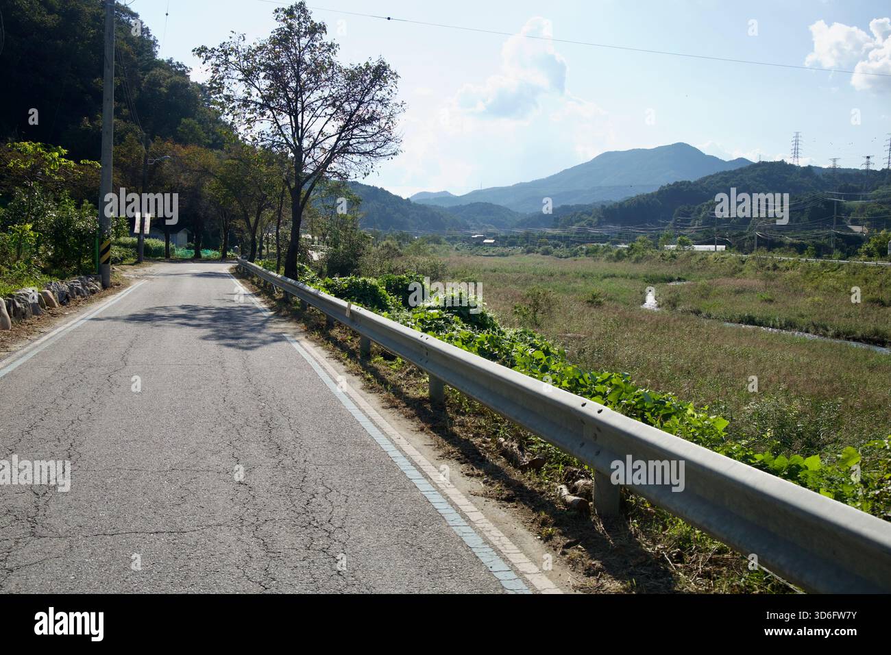 Eine ruhige Gasse folgt dem Daljeon Stream mit Schilfbeeten und weit entfernten Bergkämmen, die einen malerischen Abschnitt des Bukhangang Bike Path in Gapyeong bilden. Stockfoto
