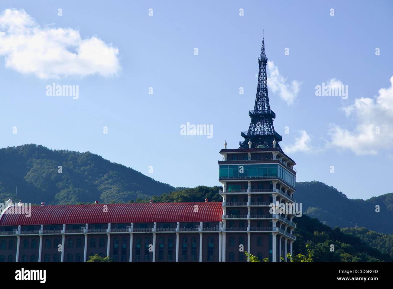 Ein Blick aus der Nähe auf den Cafe Paris Komplex in Sangcheon zeigt seinen Wahrzeichen Turm, der über einem roten Dach erhebt, inmitten von bewaldeten Hügeln und einem klaren Gebäude Stockfoto