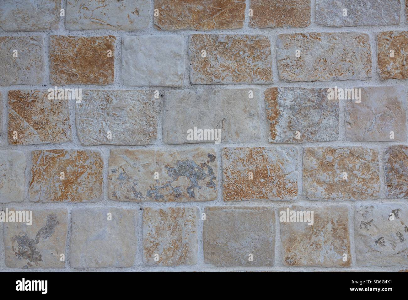 Eine verwitterte graue Steinmauer aus unregelmäßigen Felsen, die mehrschichtiges Mauerwerk und Anklänge von trockenem Gras im Vordergrund zeigt. Ideal für rustikale Architektur Stockfoto