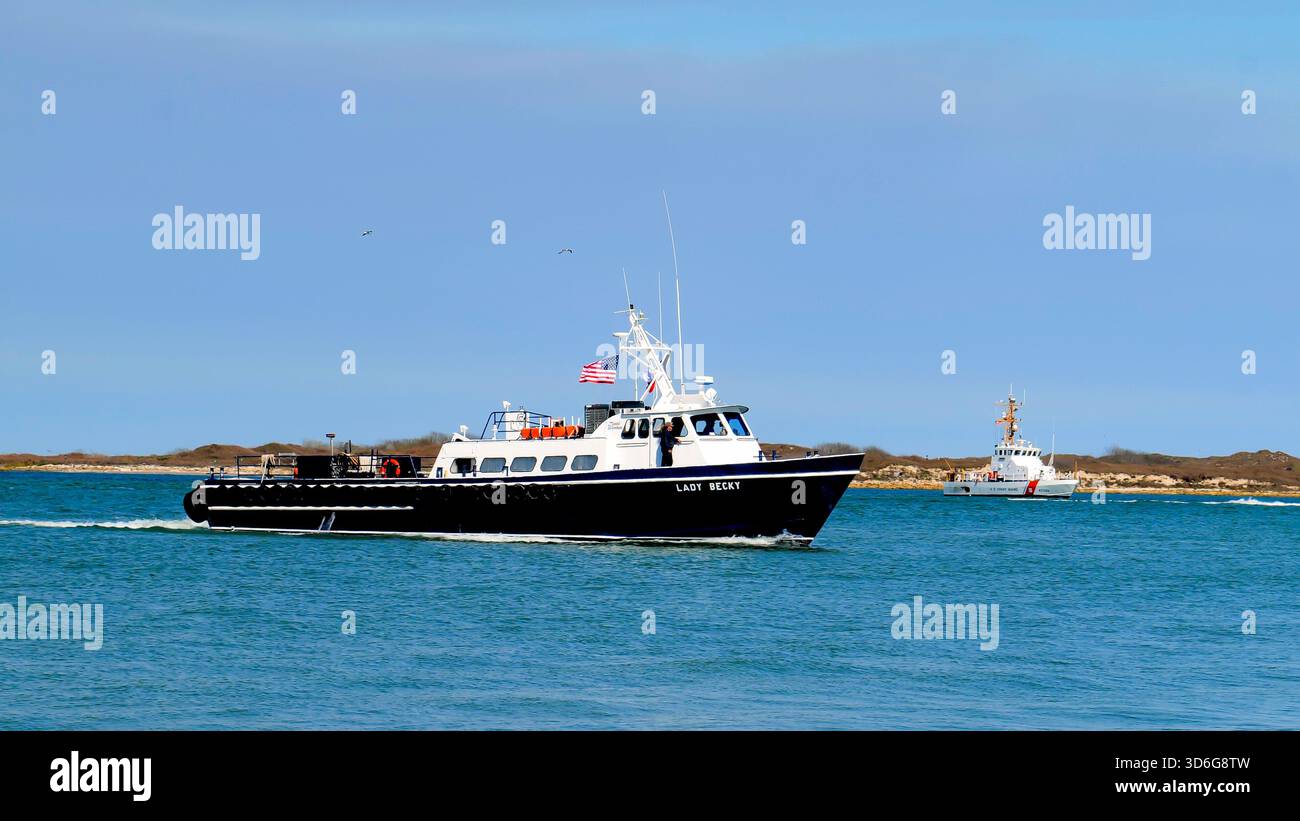 PORT ARANSAS, TX - 28. Feb 2020: Die LADY BECKY, ein kommerzielles Boot segelt an einem sonnigen Tag auf dem ruhigen blauen Wasser, mit einem Cutter der Küstenwache in der d Stockfoto