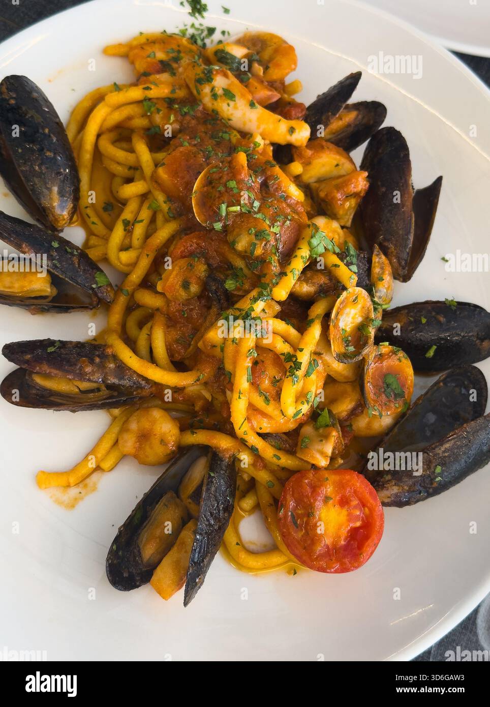 Blick auf einen runden Teller italienischer Meeresfrüchte-Pasta, garniert mit einer halben Tomate auf einem Trattoria-Tisch in Italien. Stockfoto