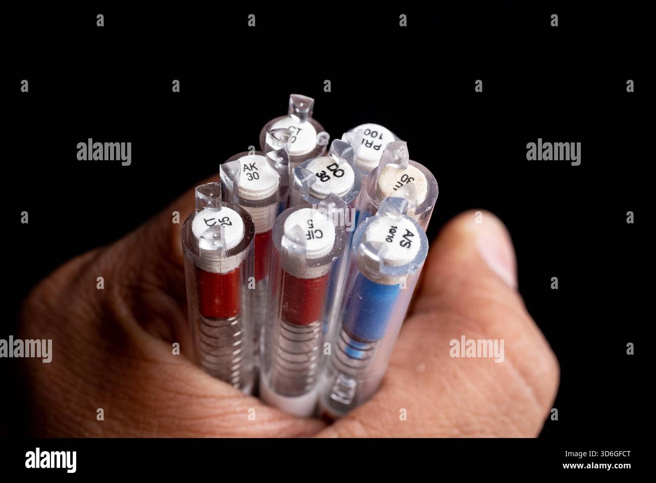Nahaufnahme einer Hand, die mehrere farbige Stifte vor schwarzem Hintergrund hält. Stockfoto