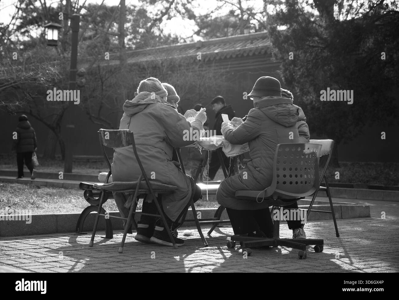 Winterkarten in einem Park in Peking, ältere Frauen genießen die Sonne in ruhigem Schwarz-weiß Stockfoto