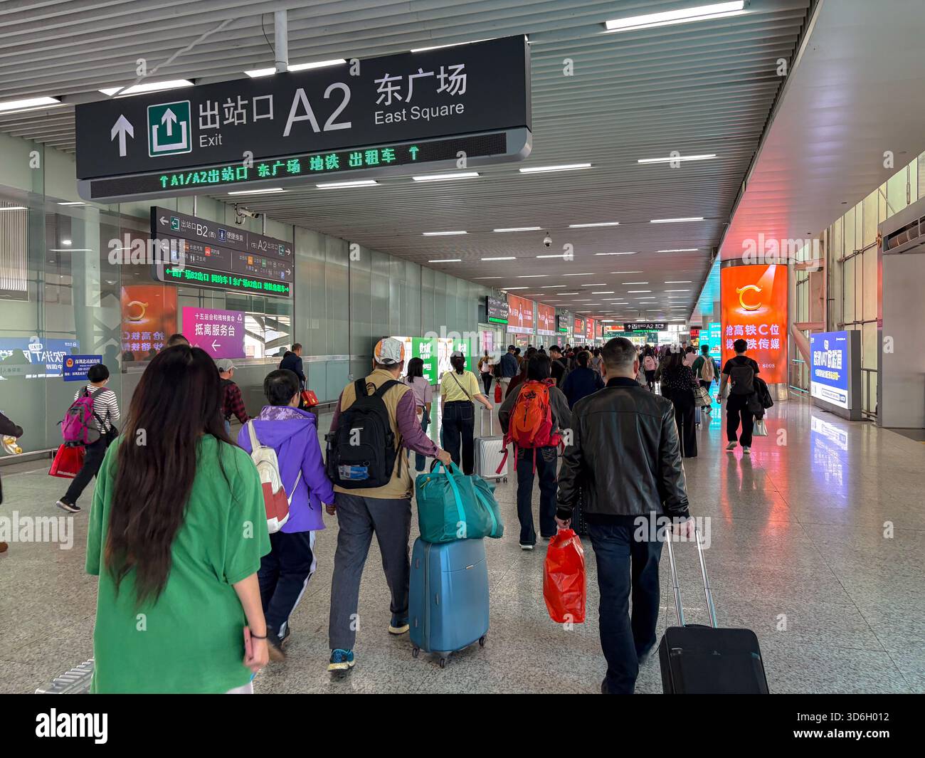 Passagiere gehen mit Gepäck durch die geschäftige Halle des Shenzhen North Railway Station, Shenzhen, China, und folgen dabei den Schildern für Ausfahrten und Plätze. Stockfoto