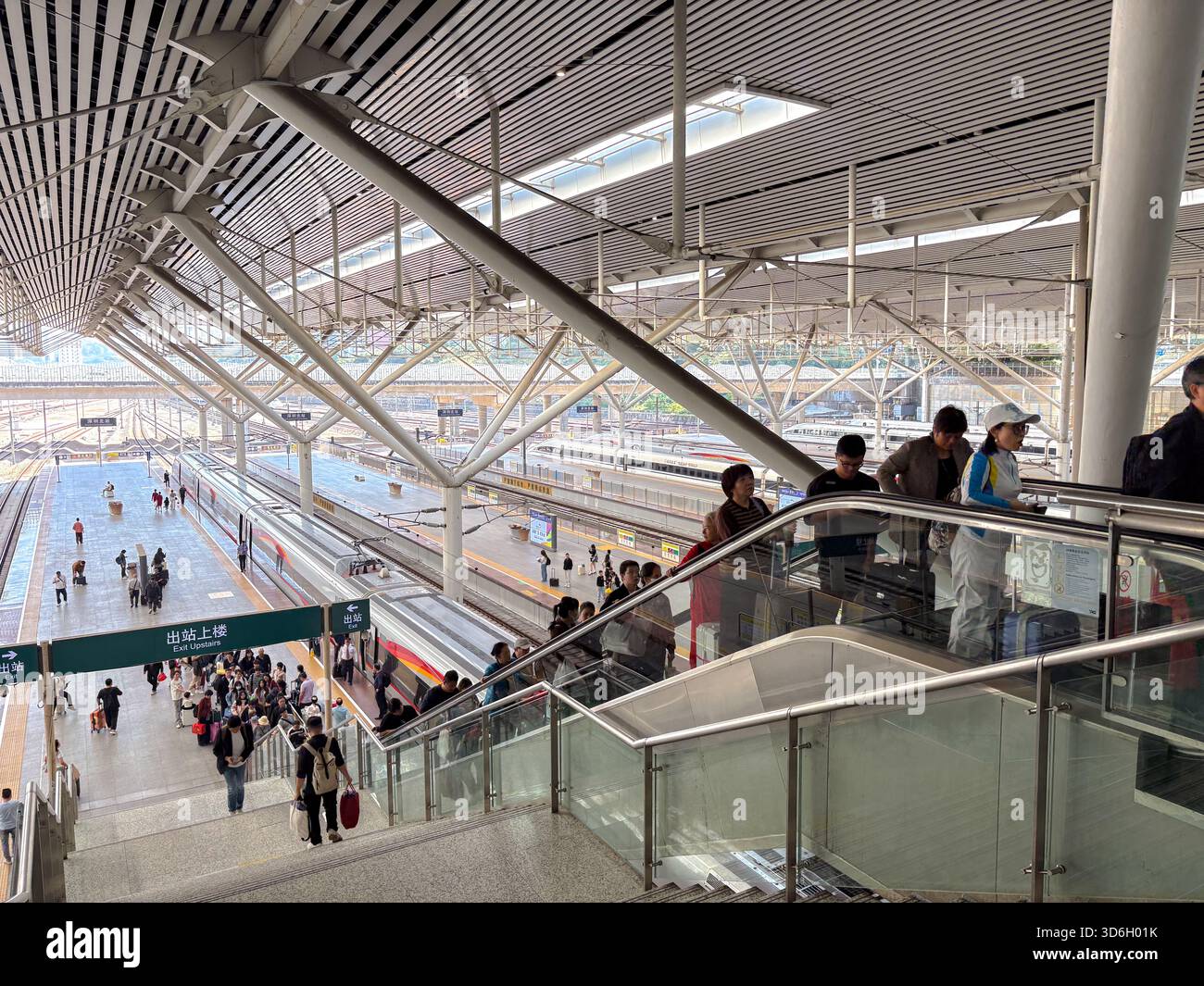Bahnhof Shenzhen North. Hochwinkelansicht von Fahrgästen auf Bahnsteigen und Rolltreppen, Hochgeschwindigkeitszüge auf Gleisen sichtbar. Stockfoto