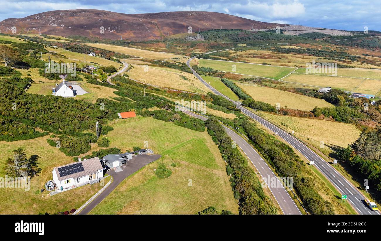 Malerische Strecke der NC500 in der Nähe von Helmsdale (Navidale), mit einer weiten Highlands Road, die in Richtung der sanften Heidekügel unter hellem Himmel führt. Stockfoto