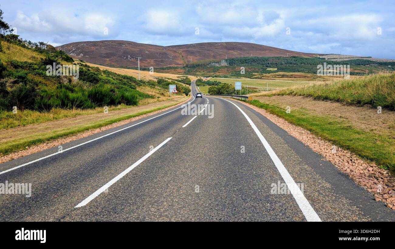 Malerische Strecke der NC500 in der Nähe von Helmsdale (Navidale), mit einer weiten Highlands Road, die in Richtung der sanften Heidekügel unter hellem Himmel führt. Stockfoto