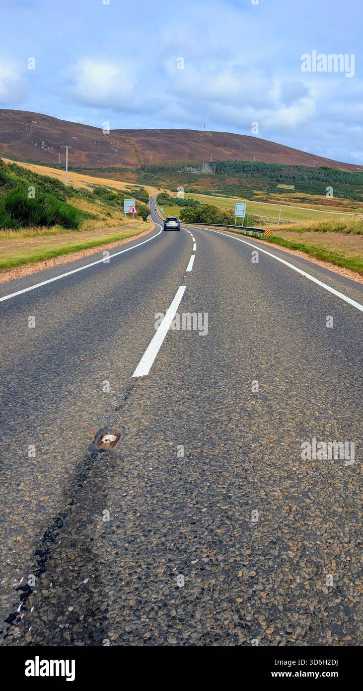 Malerische Strecke der NC500 in der Nähe von Helmsdale (Navidale), mit einer weiten Highlands Road, die in Richtung der sanften Heidekügel unter hellem Himmel führt. Stockfoto