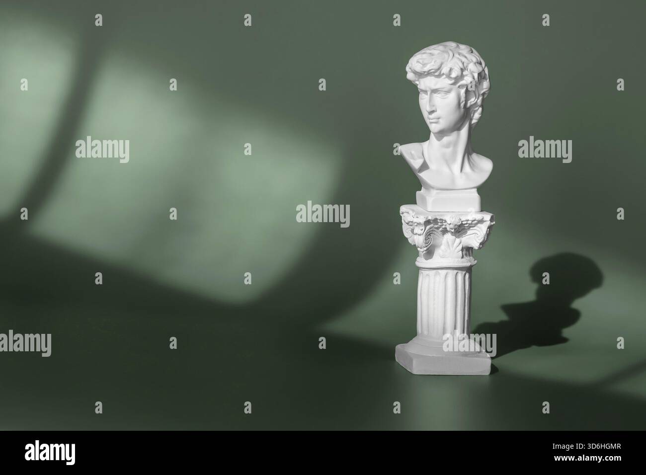 Weißer Marmorkopf des jungen Mannes, Kopf der berühmten Statue von Michelangelo - David aus Florenz. Gipskopie des alten Statuenkopfes auf grünem Hintergrund wi Stockfoto