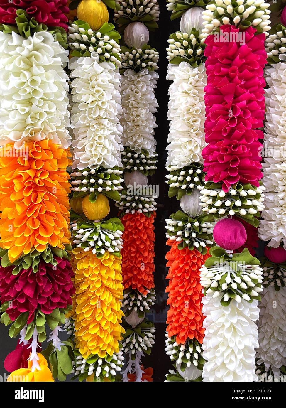 Farbenfrohe hängende Girlanden aus künstlichen Blumen in leuchtenden Farbtönen, vertikal angeordnet für traditionelle Dekoration Stockfoto