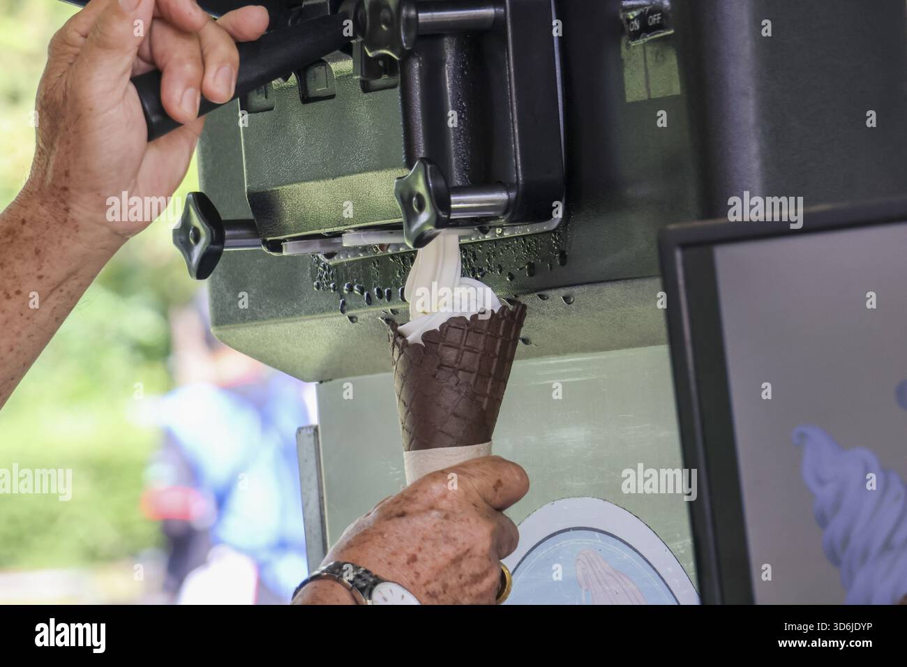 Fröhliche Seniorin serviert erfrischendes Vanilleeis aus der Maschine in Schokoladentegel. Köstliches süßes Dessert im Sommer Stockfoto